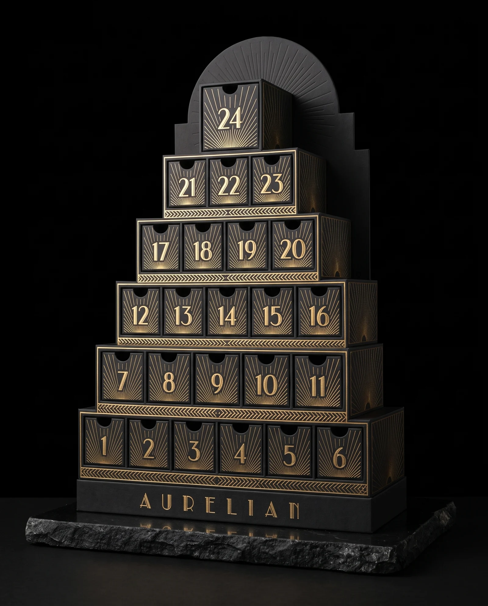 A black rigid advent calendar shaped like a stepped 1930s skyscraper: six tiers of drawers framed in mirror gold foil sunburst rays, numbered 1 to 23 rising to a single tall drawer for 24 at the crown, with AURELIAN in spaced Deco capitals on the base. Design exploration.