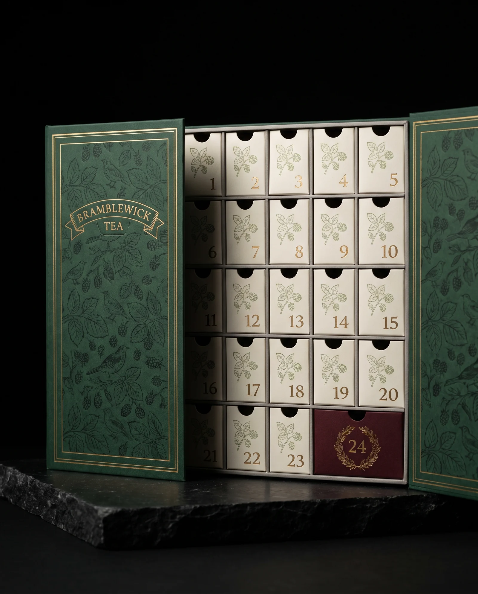 A deep green book-style advent calendar opened on two doors covered in a tone-on-tone bramble and thrush pattern with matte antique gold rules and a ribbon banner reading BRAMBLEWICK TEA; inside, 23 cream drawers with gold numerals and a double-width oxblood drawer 24 with a gold wreath.