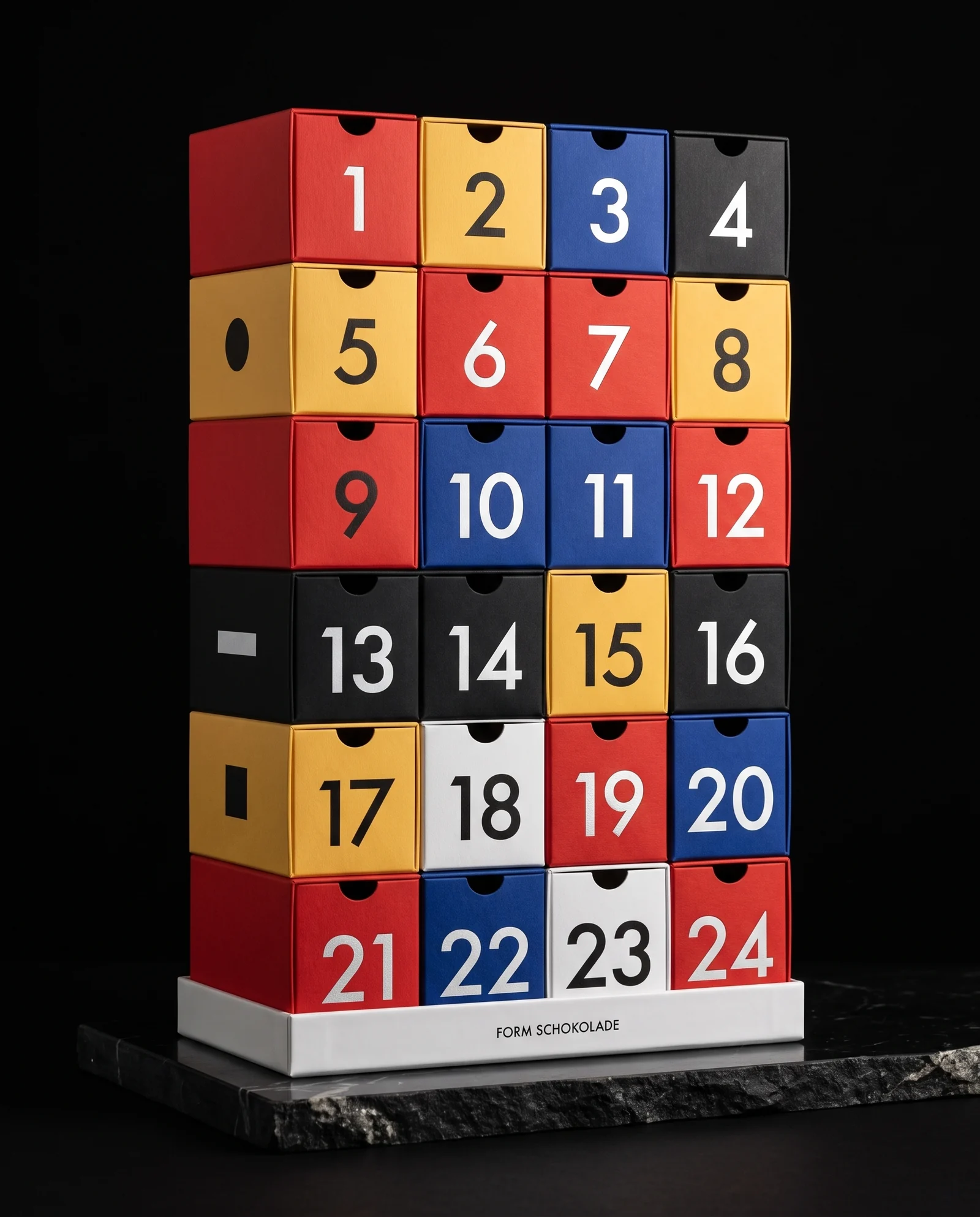 An advent calendar made of 24 separate small boxes in red, yellow, blue, black and white stacked in six rows on a white tray marked FORM SCHOKOLADE, each with a large geometric numeral from 1 to 24.