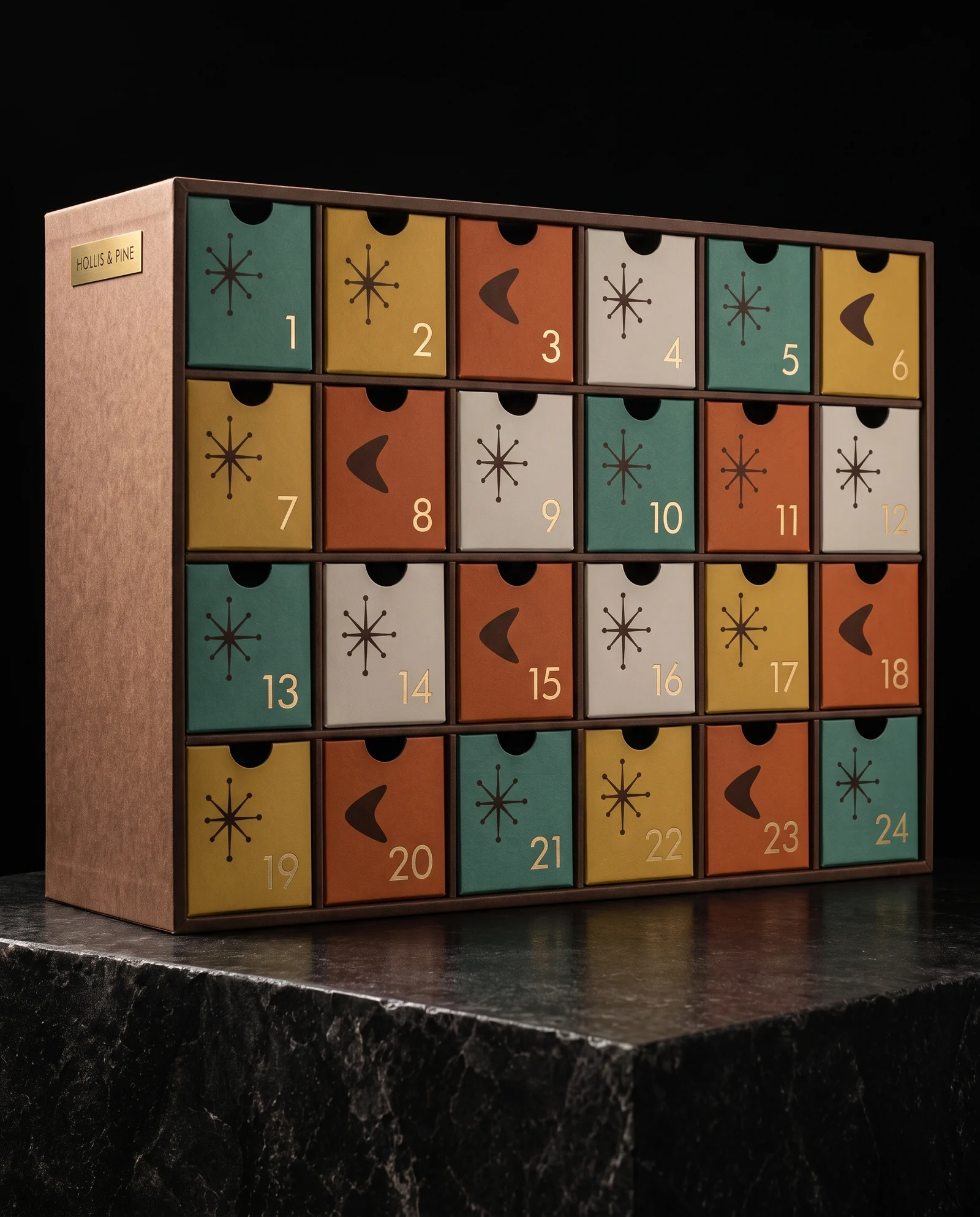 A low walnut-brown advent calendar cabinet with 24 drawers in teal, mustard, burnt orange and off-white, each with a dark brown atomic starburst or boomerang and a matte gold numeral, and a small gold plate reading HOLLIS & PINE.