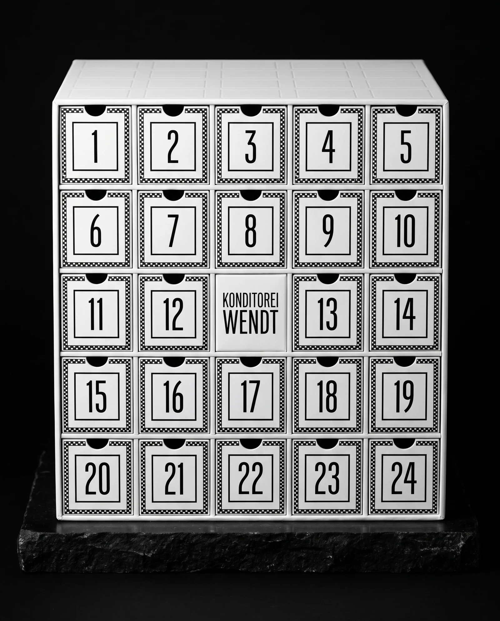 A white cube-shaped advent calendar with a five-by-five grid of square drawers framed in black checkerboard borders and tall narrow black numerals, a central plate reading KONDITOREI WENDT and a blind debossed grid on the lid.