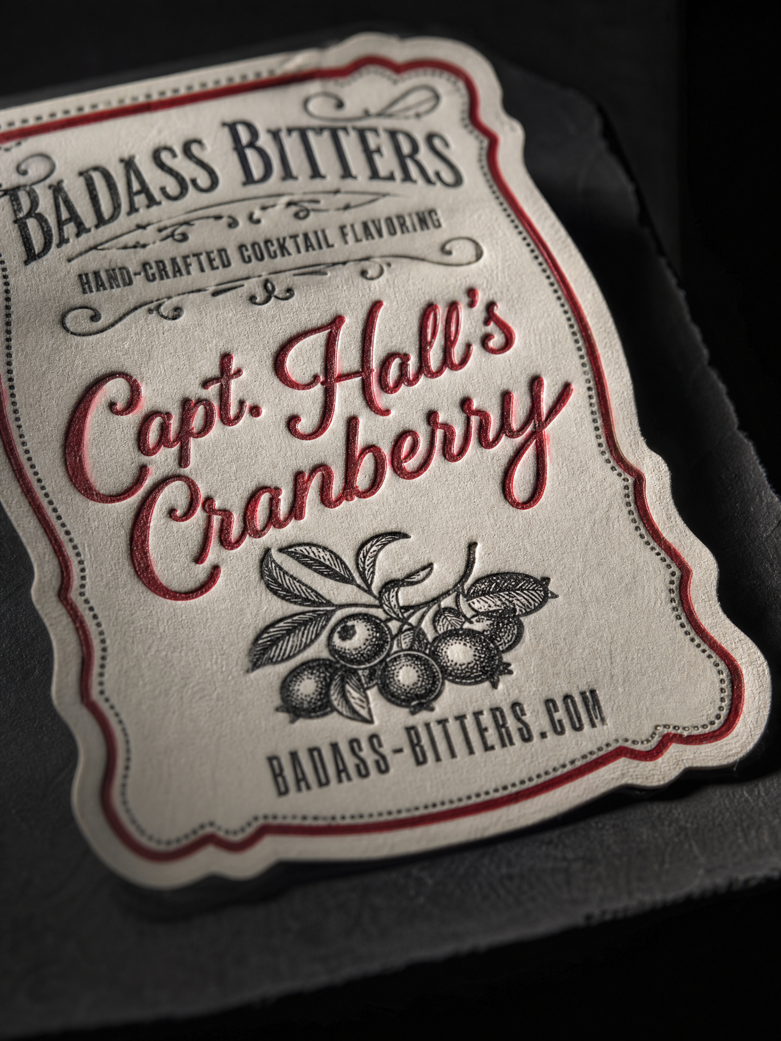 Macro: the letterpress impression of the hand-lettered flavour name in the cream label stock, the scalloped kiss-cut edge and the accent colour