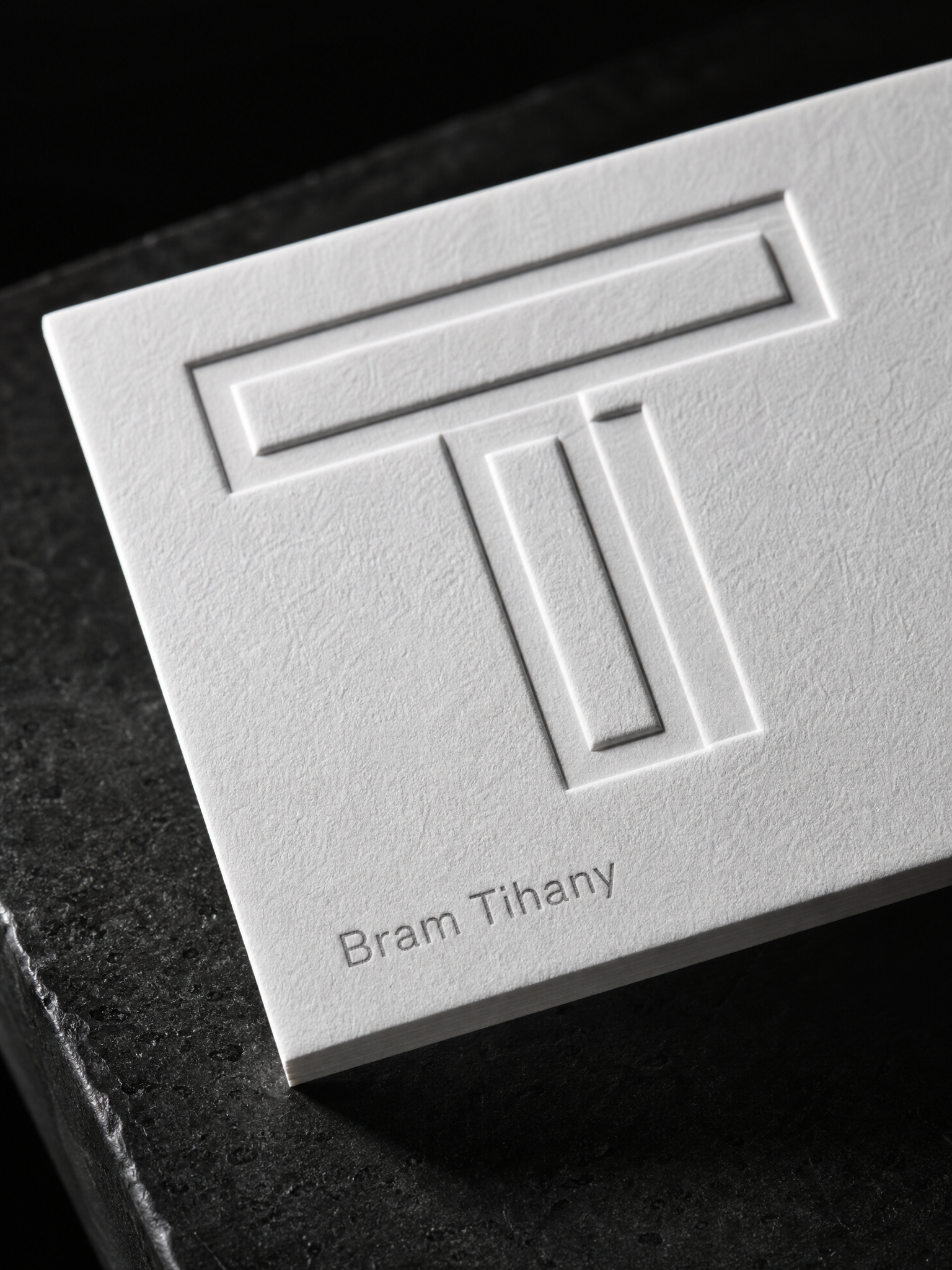 Macro: the multi-level embossed T monogram rising from the white cotton, each level casting its own shadow