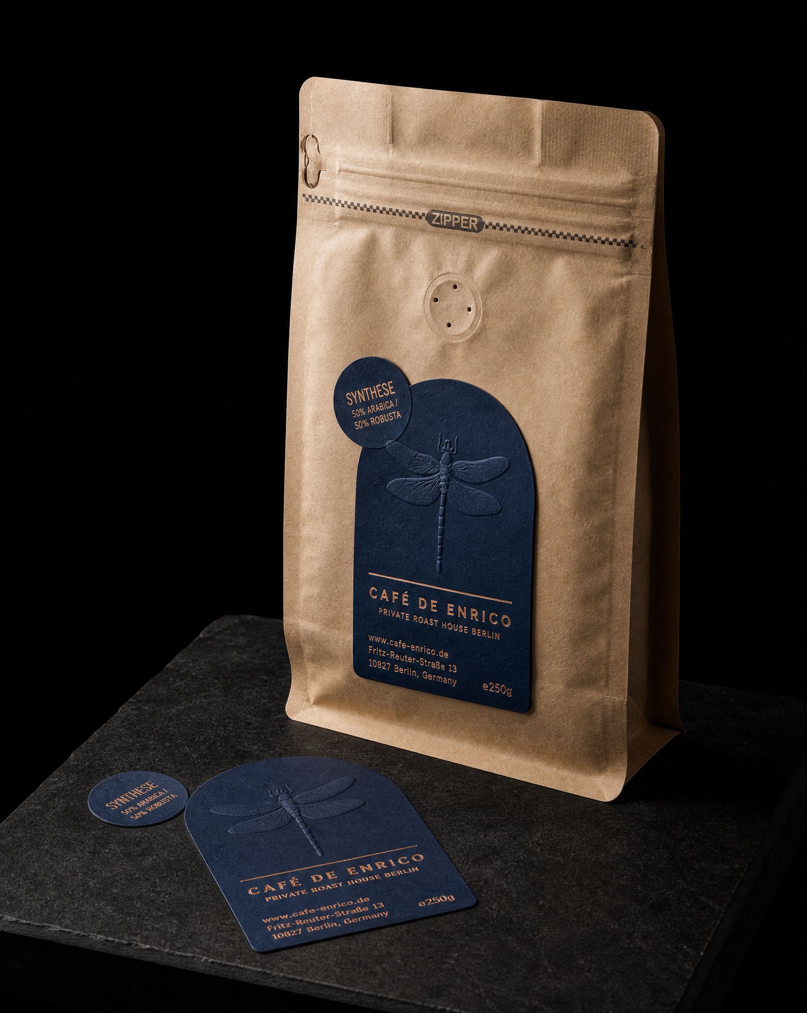 Labels for Café de Enrico, Berlin with look 2: arch die-cut label, blue uncoated, multi-level blind emboss + copper foil stamping, 250g kraft stand-up pouch, existing hardware, look 1: 1-colour direct print + blind-deboss hang tag and look 3: full-height banderole, tone-on-tone spot gloss + letterpress chip labels.
