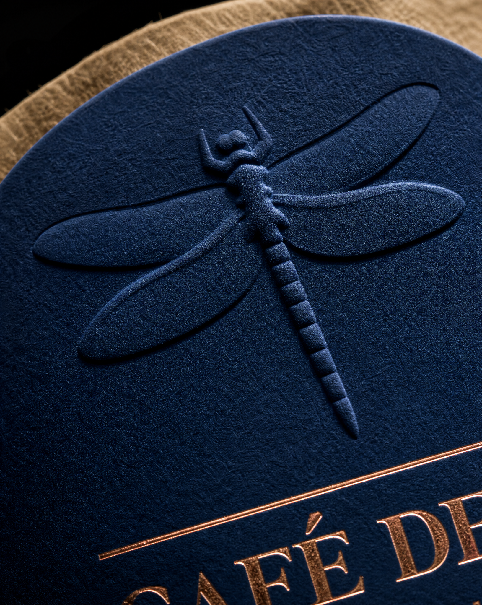 Macro of a multi-level blind embossed dragonfly and copper foil on deep blue uncoated label stock