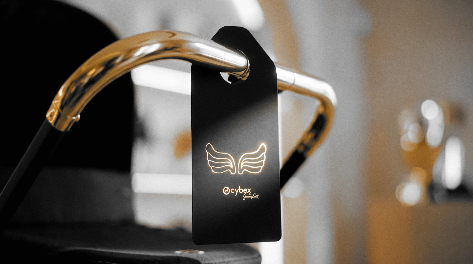The black and gold hang tag hanging through its oval slot from a gold stroller handlebar in a warm, softly lit store