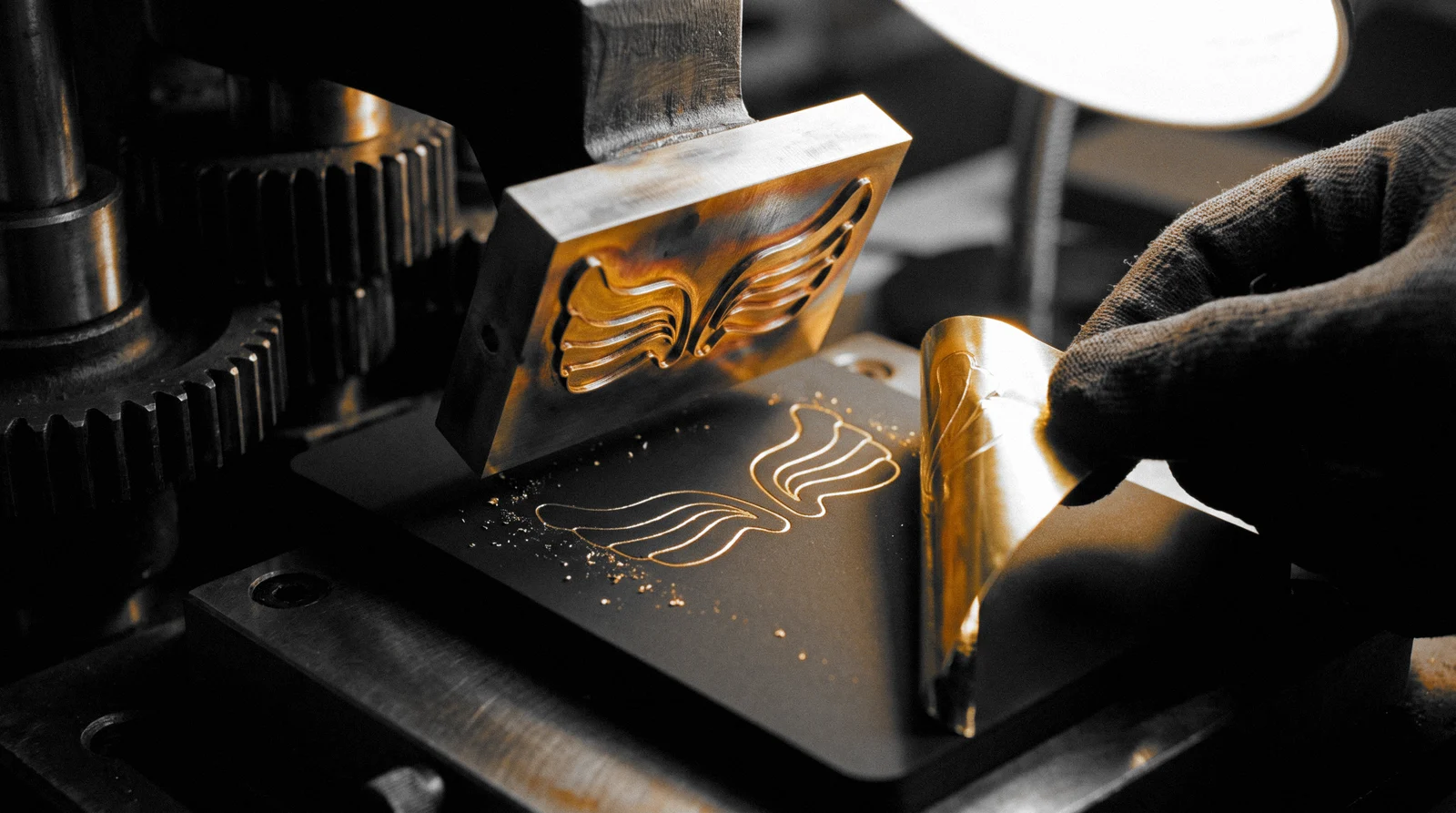 A heated brass die with the wings relief lifting off black board, the gold foil carrier film being peeled back to show the stamped wings