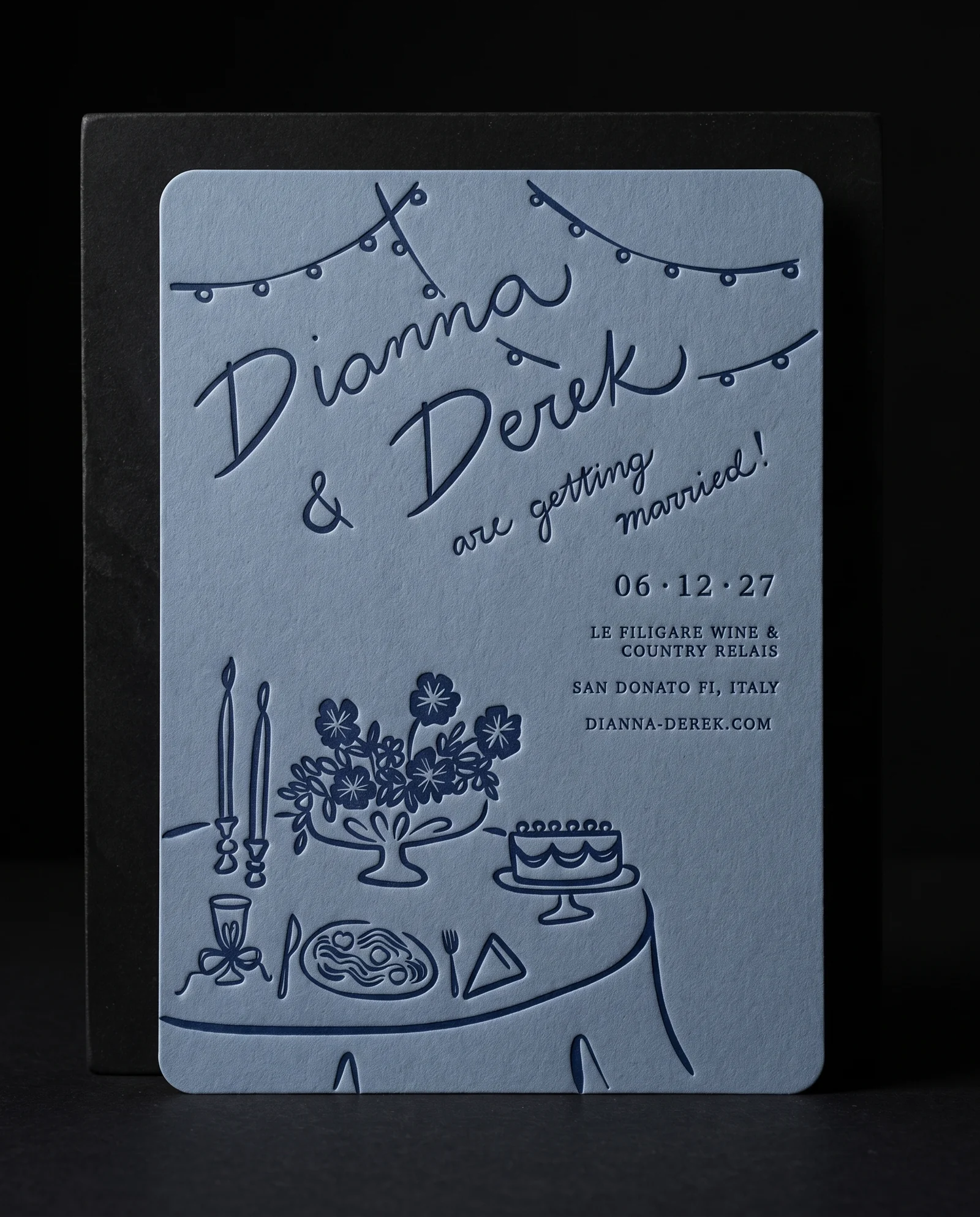 Dusty-blue invitation with navy table scene and letterpress impression on a black plinth, simulated before press