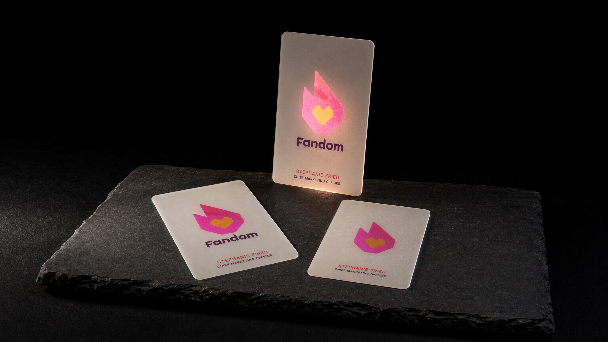 Three Fandom frosted plastic cards, one lit from behind so only the translucent flame logo glows