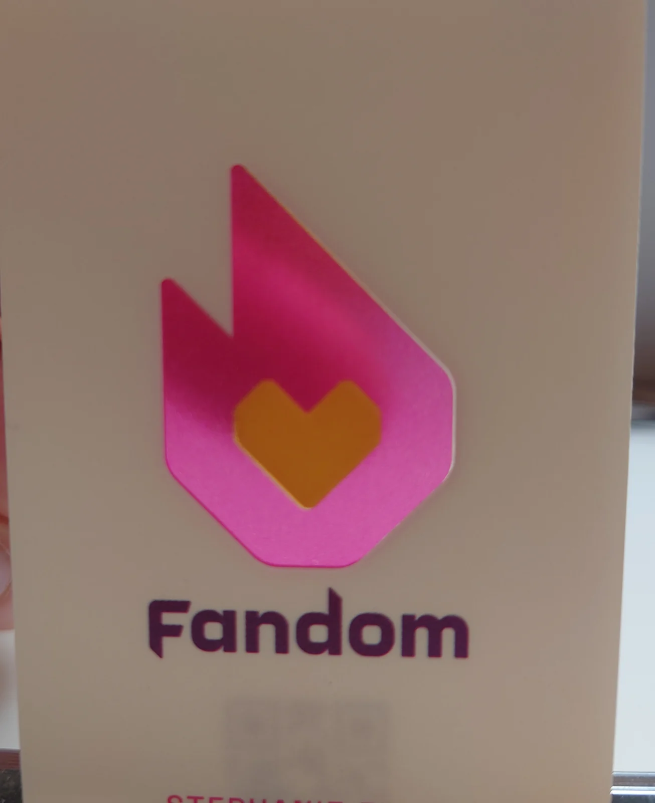 Close photograph of the finished cream Fandom card: glossy magenta flame, solid amber heart, plum wordmark