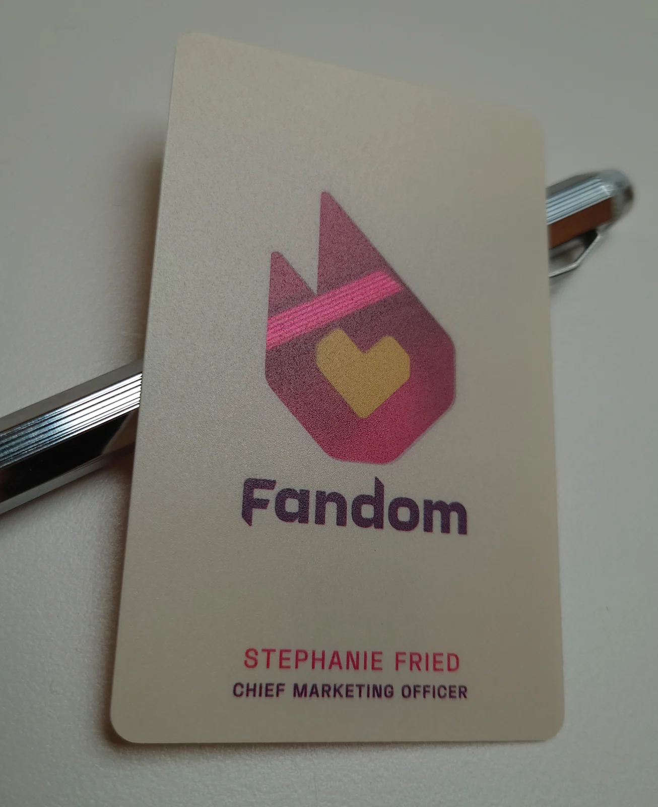 Photograph of the finished Fandom frosted plastic card with a pen lying behind it; the pen shows through the magenta flame as a pink band and nowhere else