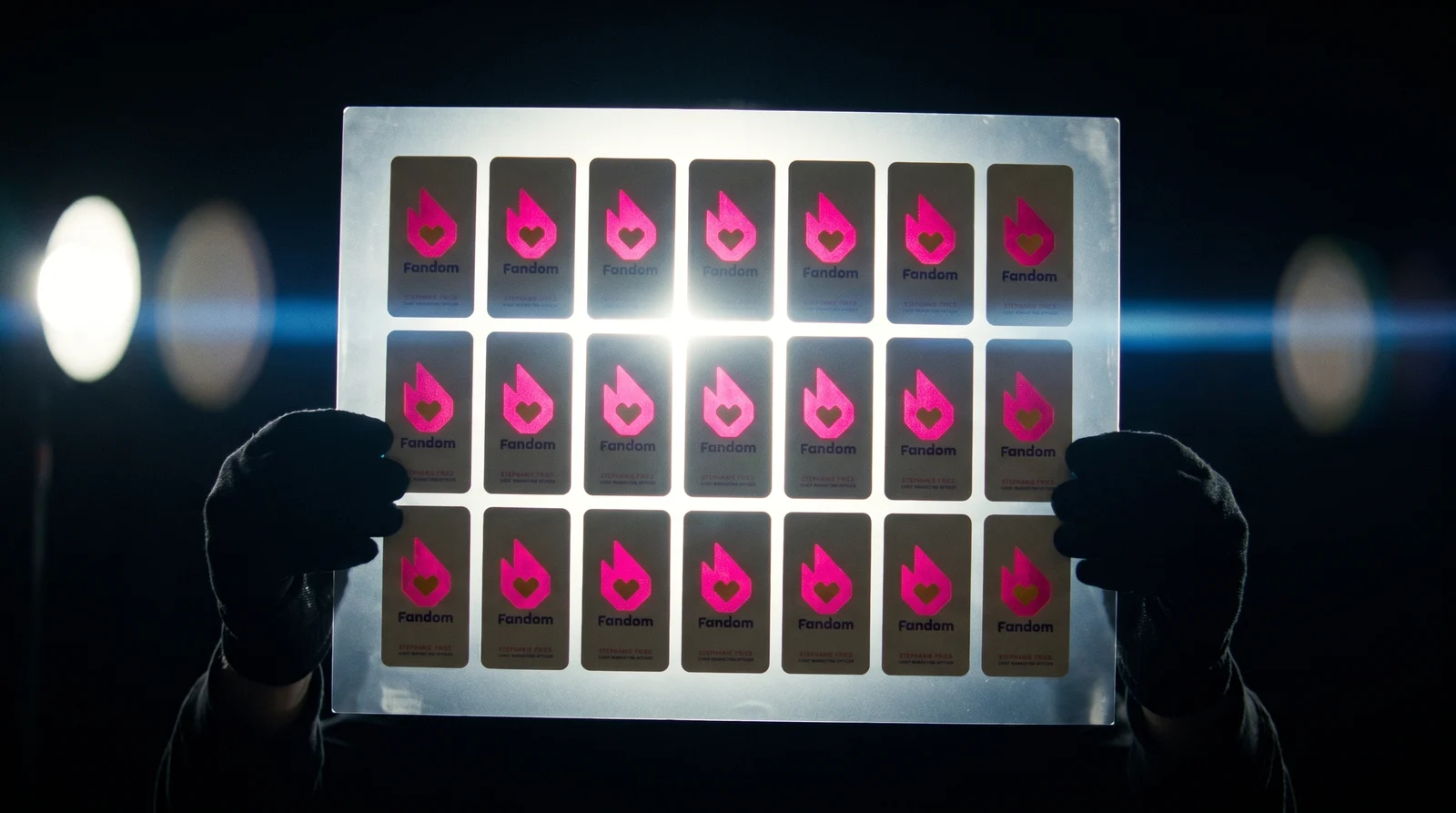 A printed sheet of 21 Fandom cards held up to a light before cutting; every flame glows magenta while the cream fields stay solid