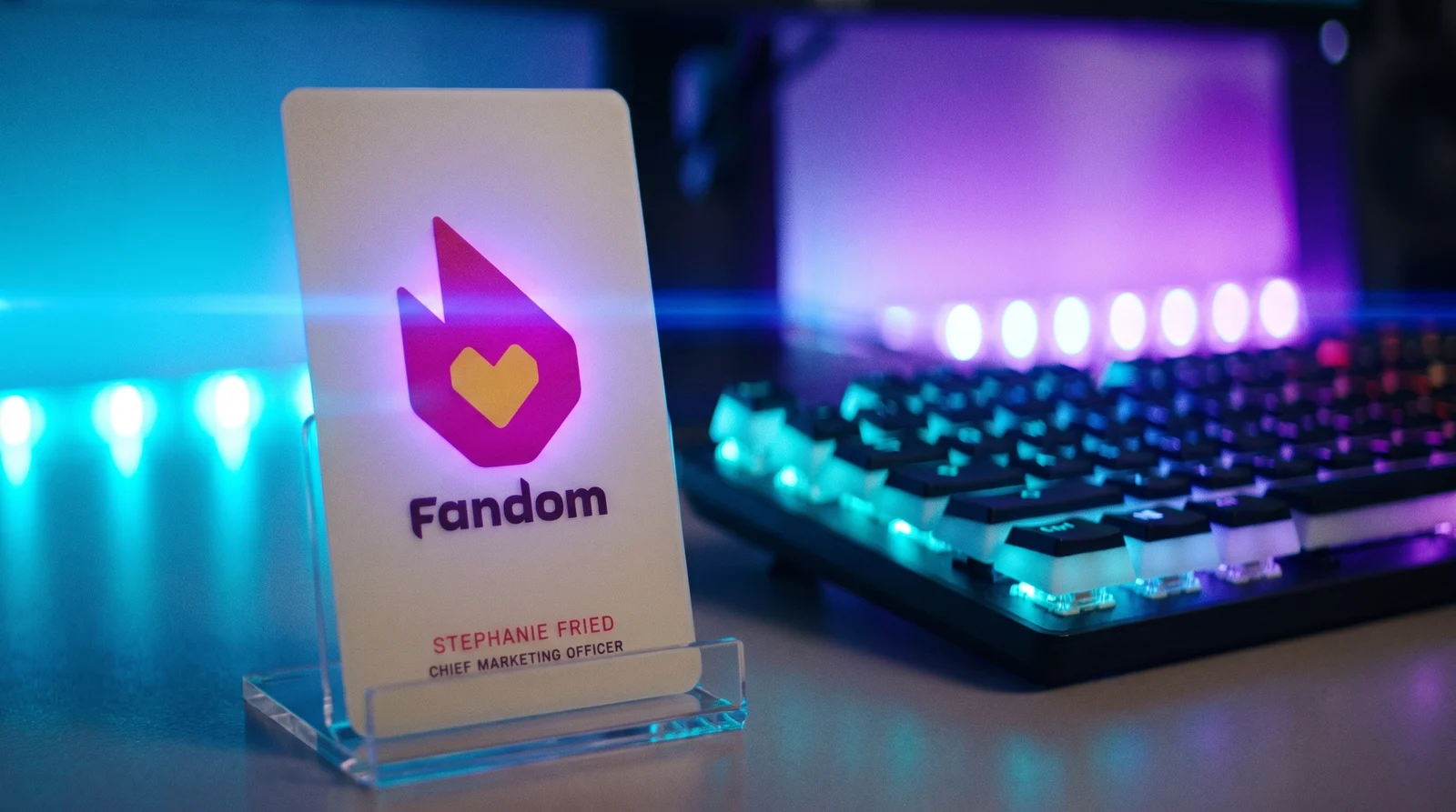 The Fandom card in a clear stand on a gaming desk; cyan and violet RGB light behind it tints the glowing flame