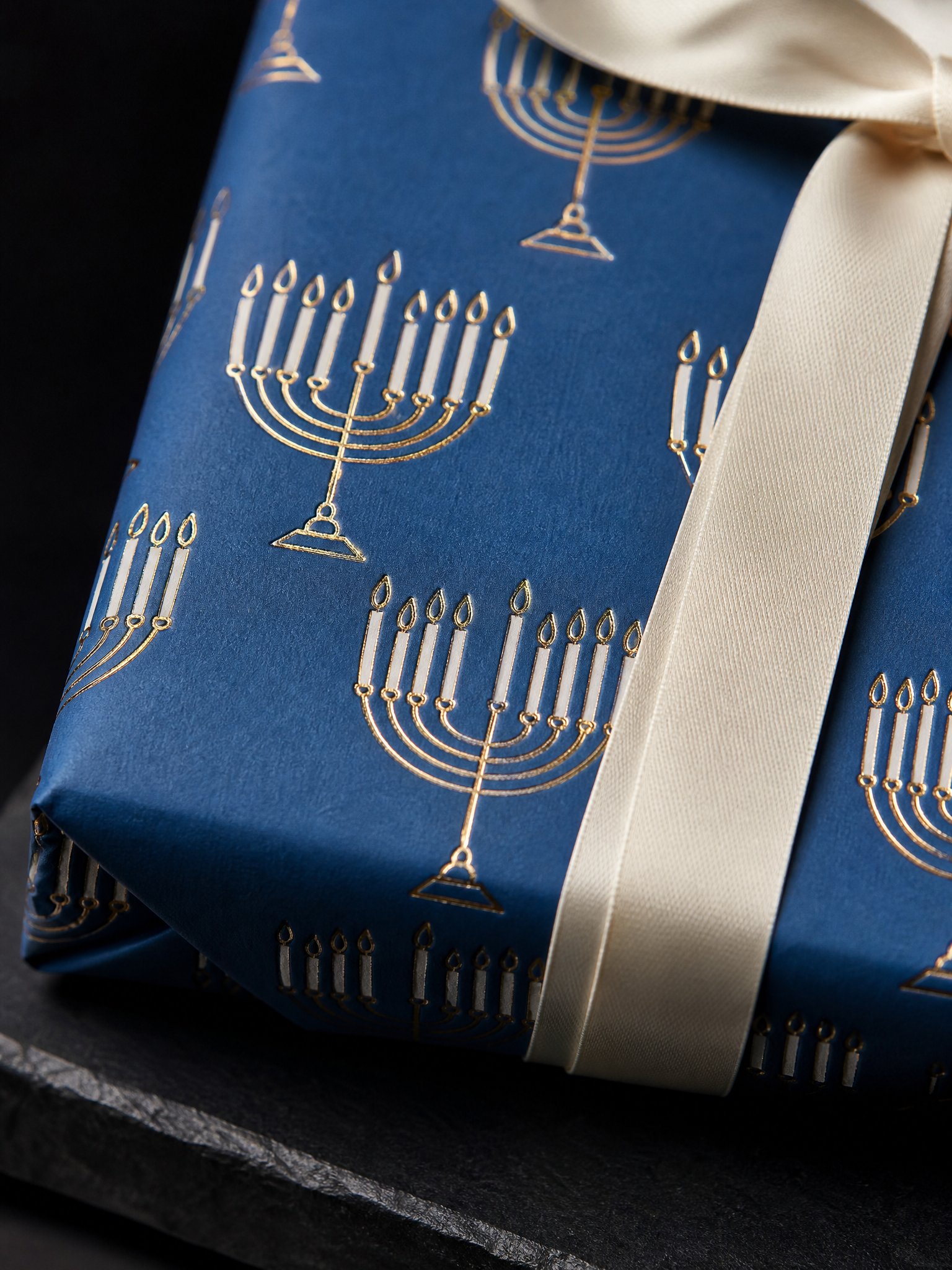 Macro: the gold foil menorah linework recessed into the blue uncoated stock, the repeat visible, paper tooth around the foil