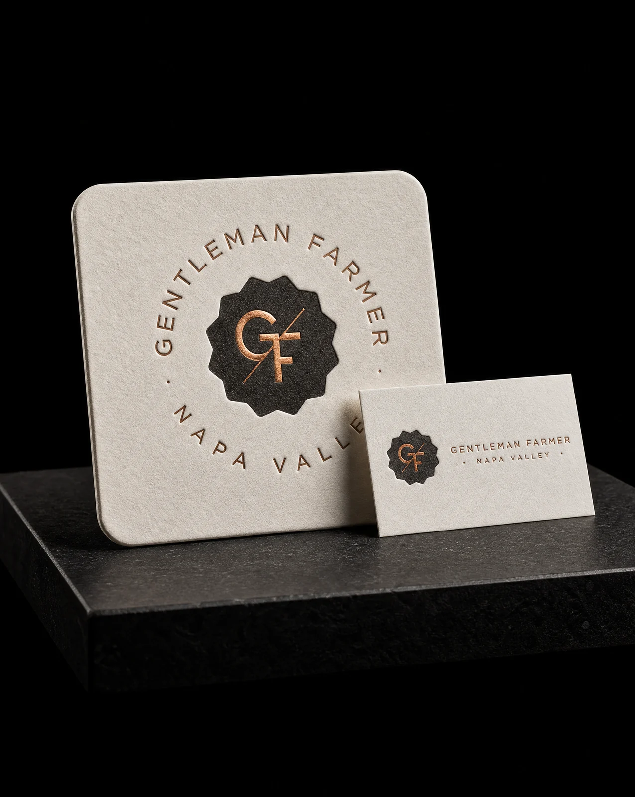 The Gentleman Farmer coaster standing beside the business card it was matched to, both in black letterpress with a copper foil monogram