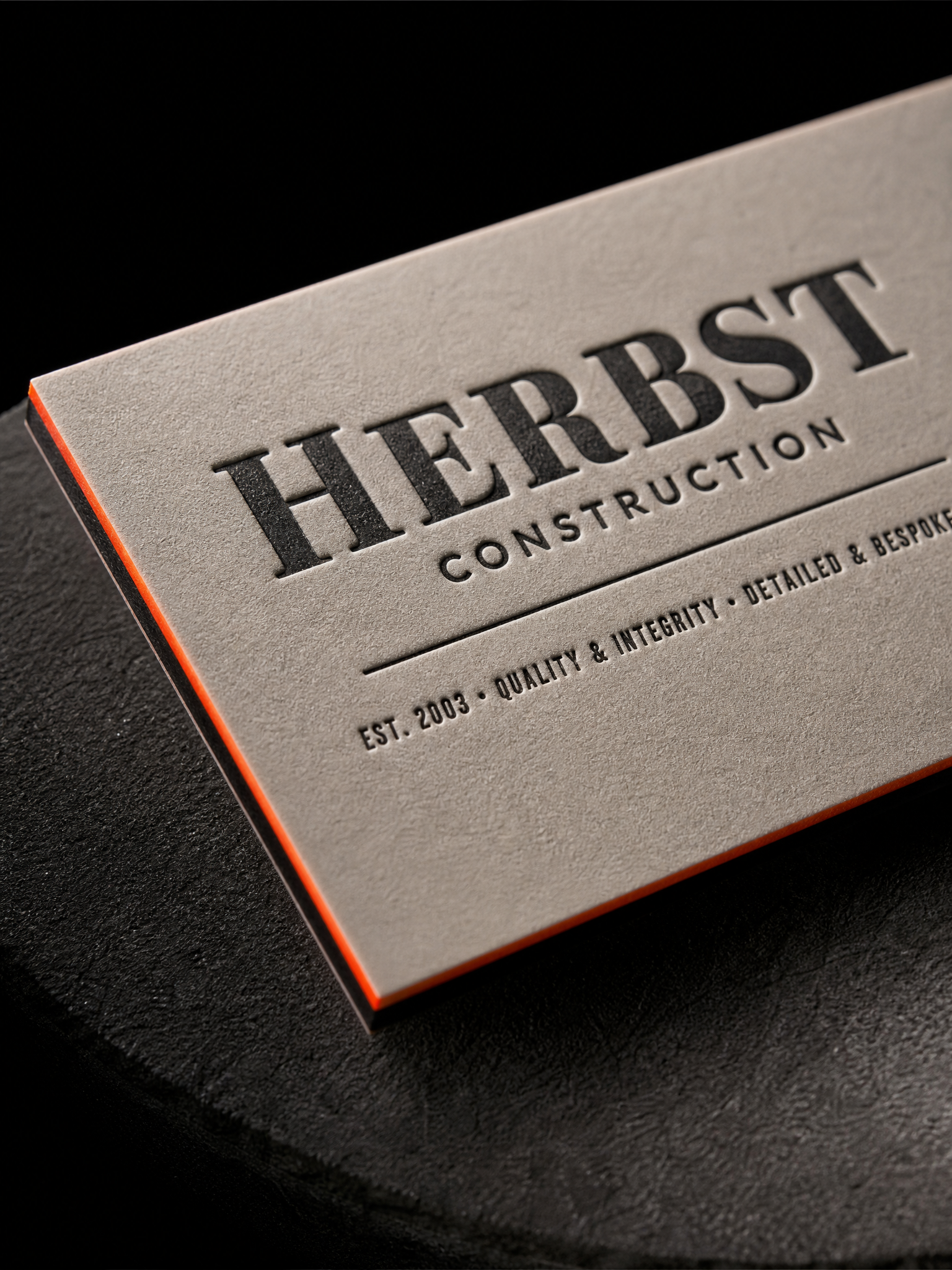 Macro: the slab-serif letterpress impression on the grey face, the safety-orange edge, the black duplex layer