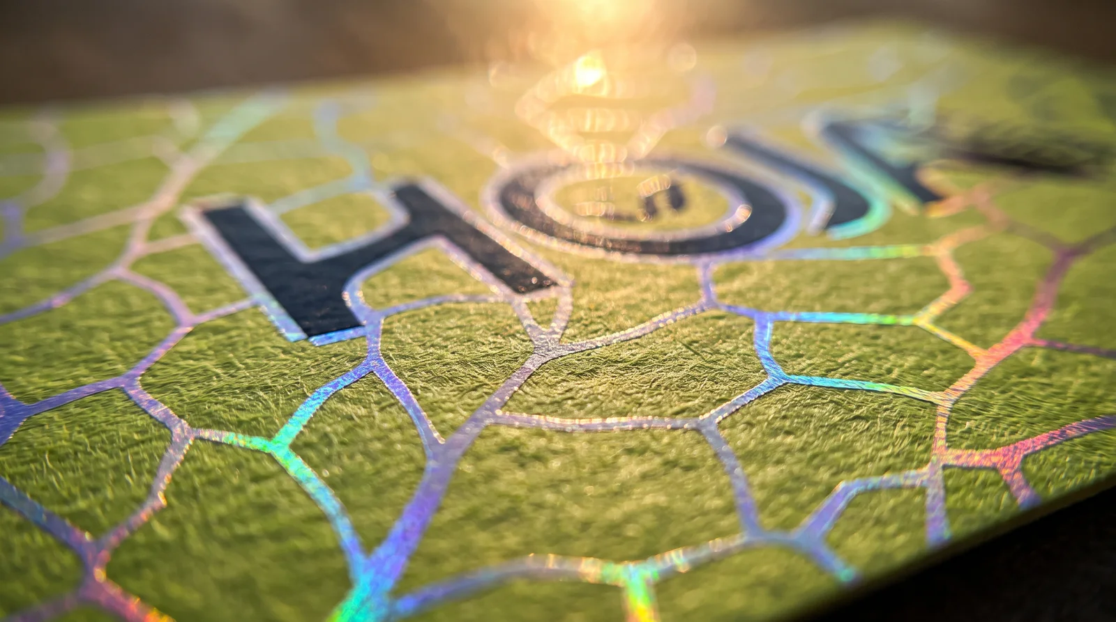Macro of the card surface: holographic foil leaf veins pressed into lime-green cotton paper, flashing violet, cyan and gold