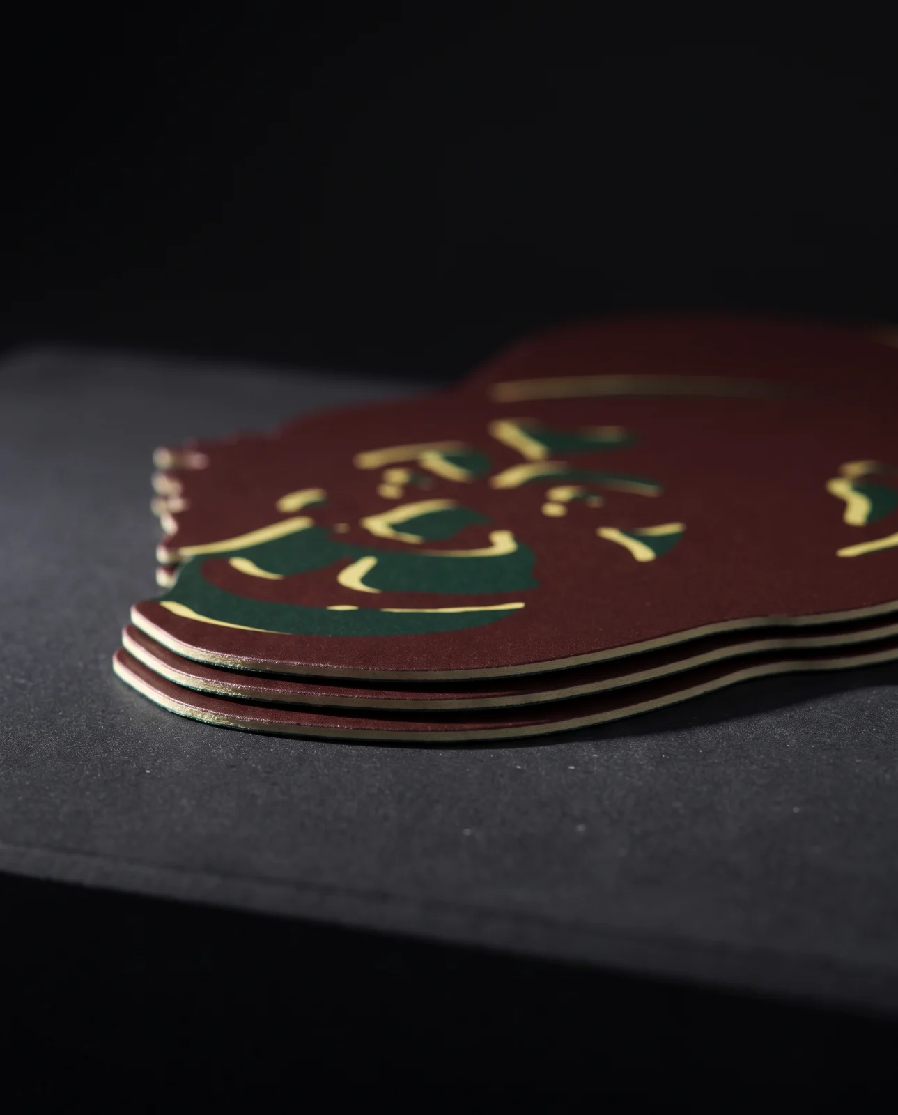 Low macro of four stacked Jay Kos die-cut cards on black stone, raking light along the cut edges of the bowler hat brim