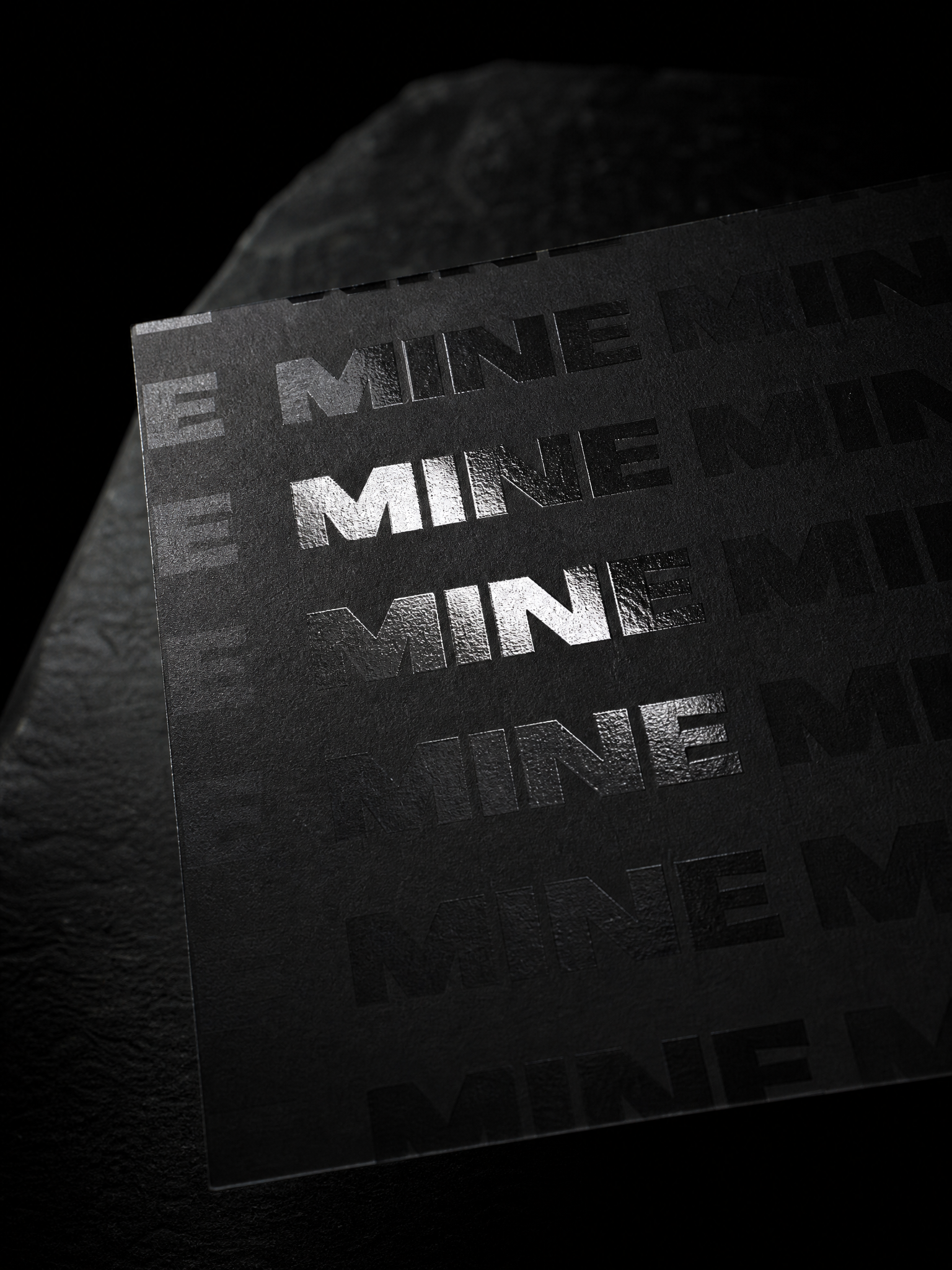 Macro: the glossy spot varnish MINE letters catching one streak of light against the matte black