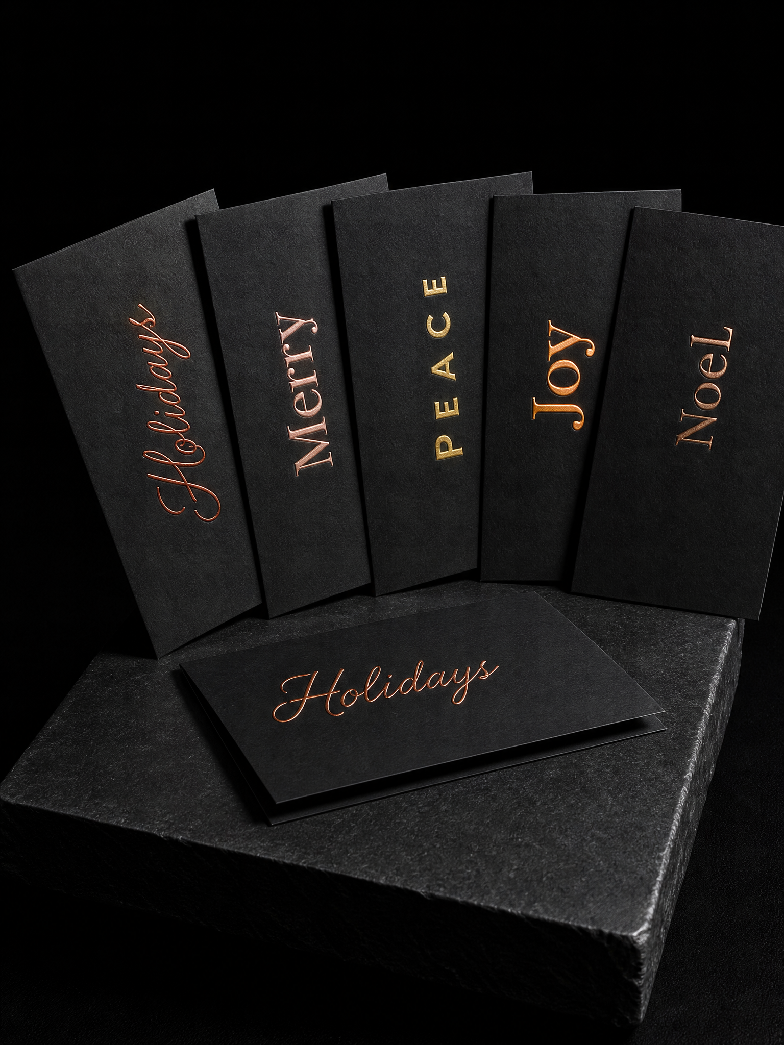 Notecards for Print Peppermint design exercise with five folded notecards fanned, 32pt black cotton, each with one word in different warm : "holidays" in copper script, "merry" in rose gold blind-emboss-plus- , "peace" in matte gold caps, "joy" in amber pigment , "noel" in bronze foil stamping.