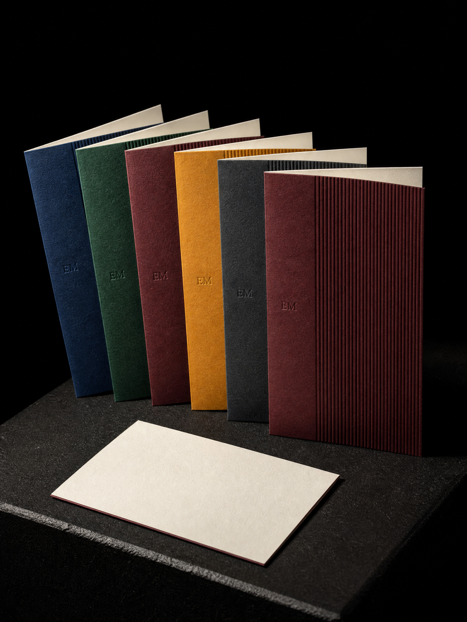 Notecards for Print Peppermint design exercise with a fan of 6 folded notecards a6, each duplexed: a ribbed-embossed face in colorplan cobalt, emerald, mulberry, amber, slate, claret bonded to a smooth cream ; the ribbing covers the right half only, with a tiny blind-debossed monogram "em" at the seam.