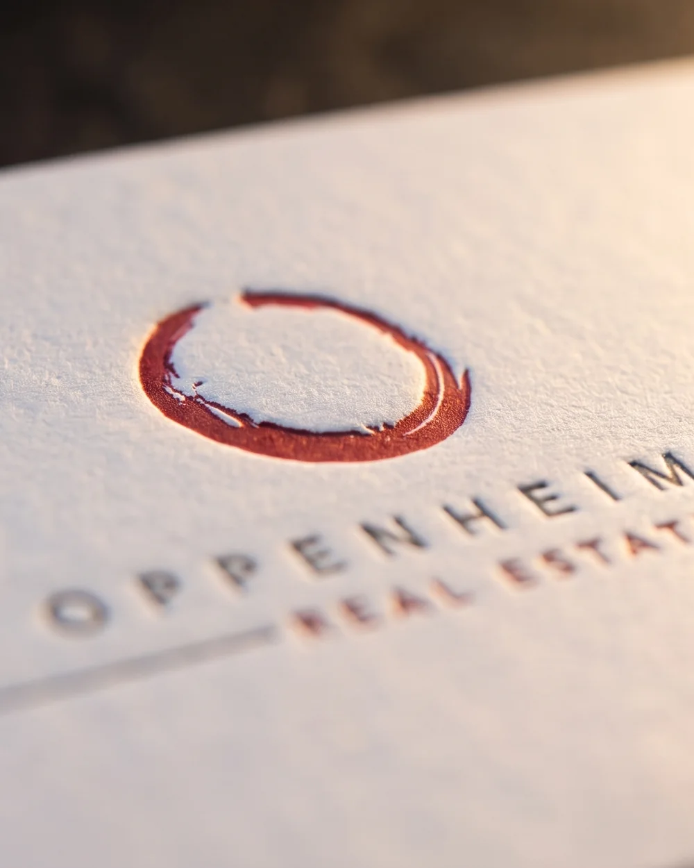 Gros plan sur le recto de la carte : l'ensō rouge et THE OPPENHEIM GROUP imprimés en creux dans le coton blanc
