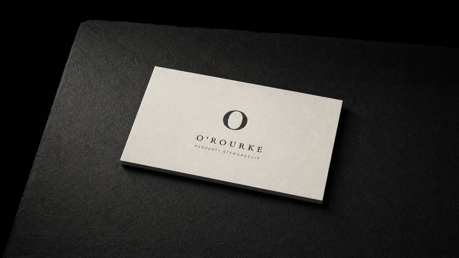 The printed O'Rourke card on warm bone, one PMS black letterpress on duplexed cotton with the dark core showing at the edge