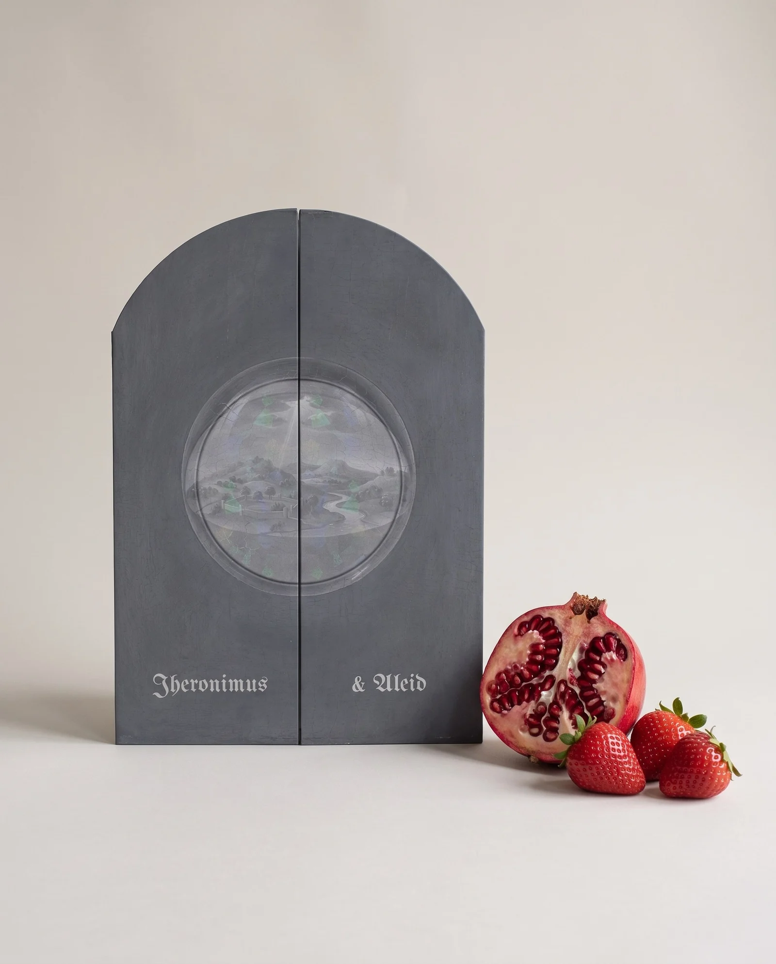 The closed triptych invitation in slate-grey paper, with an arched top, a debossed globe and platinum blackletter names