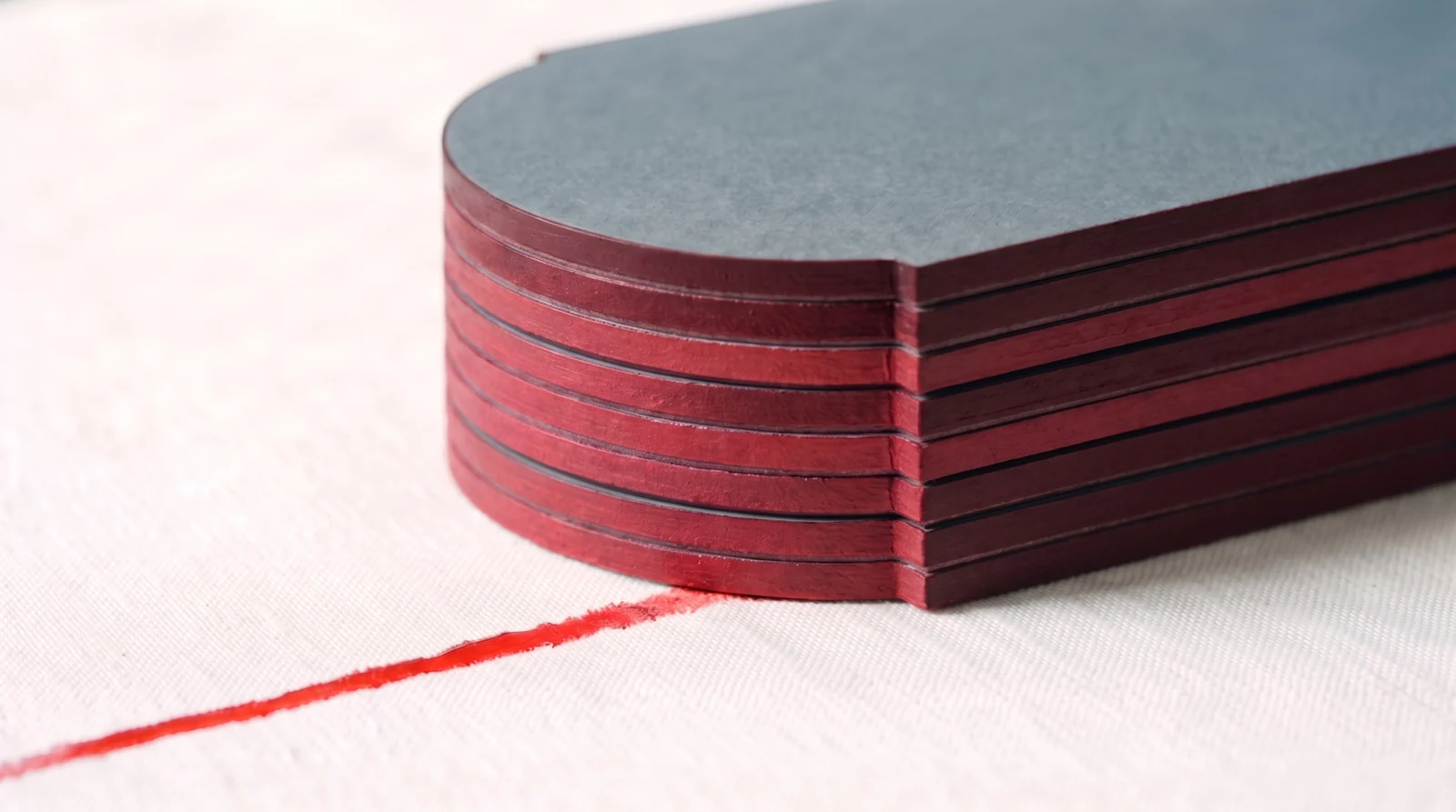 A stack of duplexed invitations with painted edges: dark maroon over the slate ply, brighter wine red over the white ply, a fine seam between