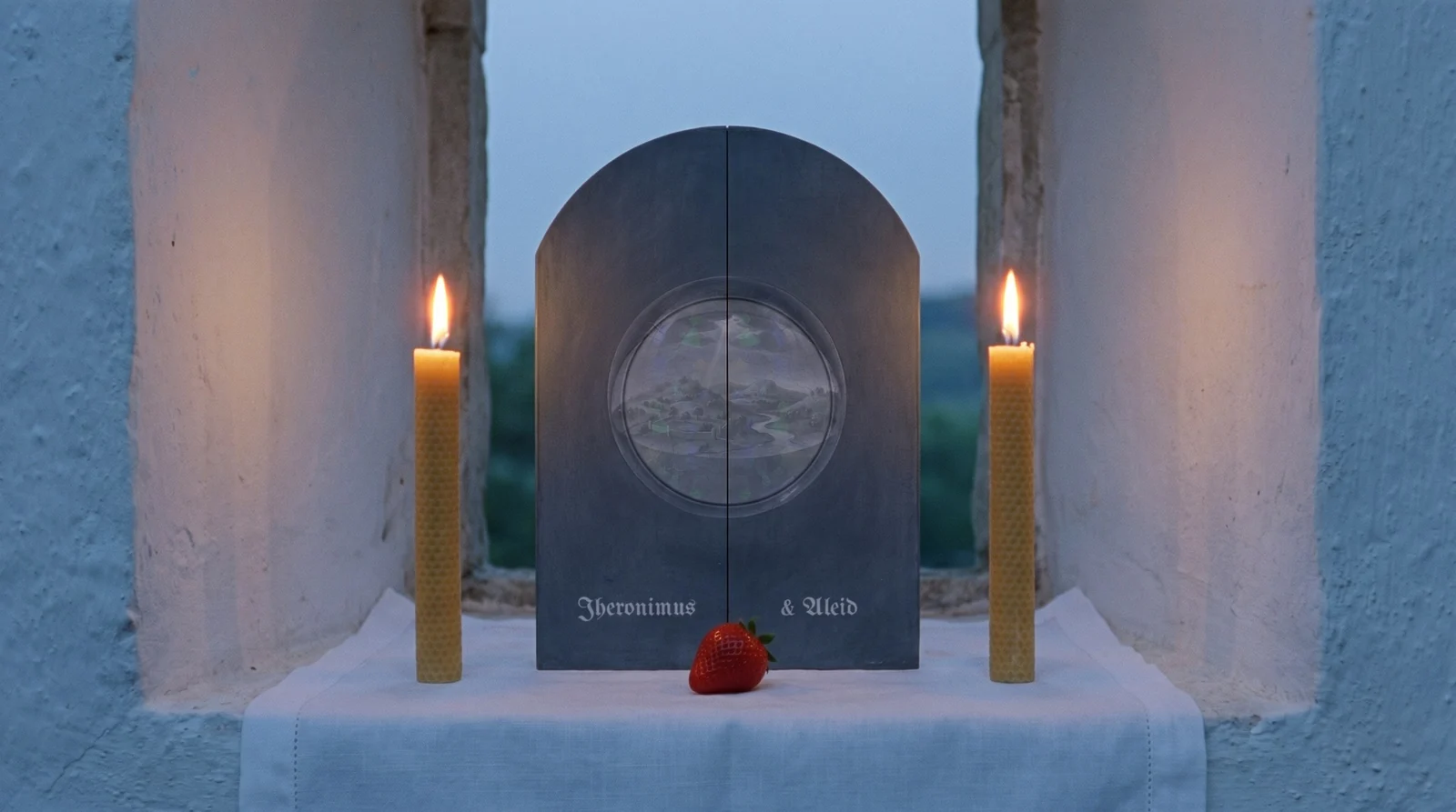 The closed invitation between two beeswax candles at dusk