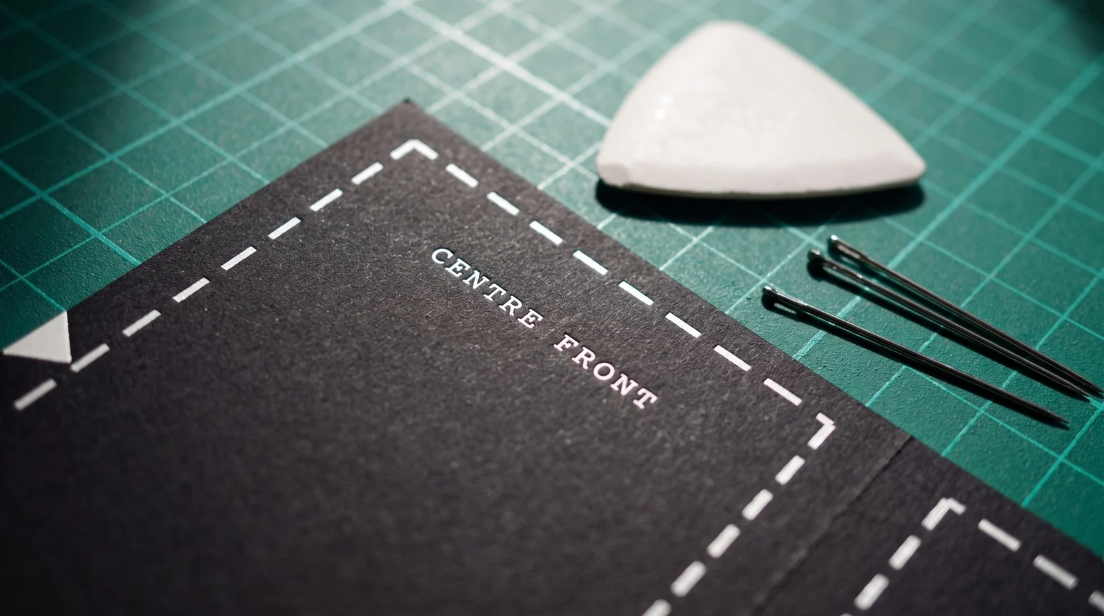 Macro of white foil seam allowance and the words CENTRE FRONT on black paper, beside tailor's chalk and pins
