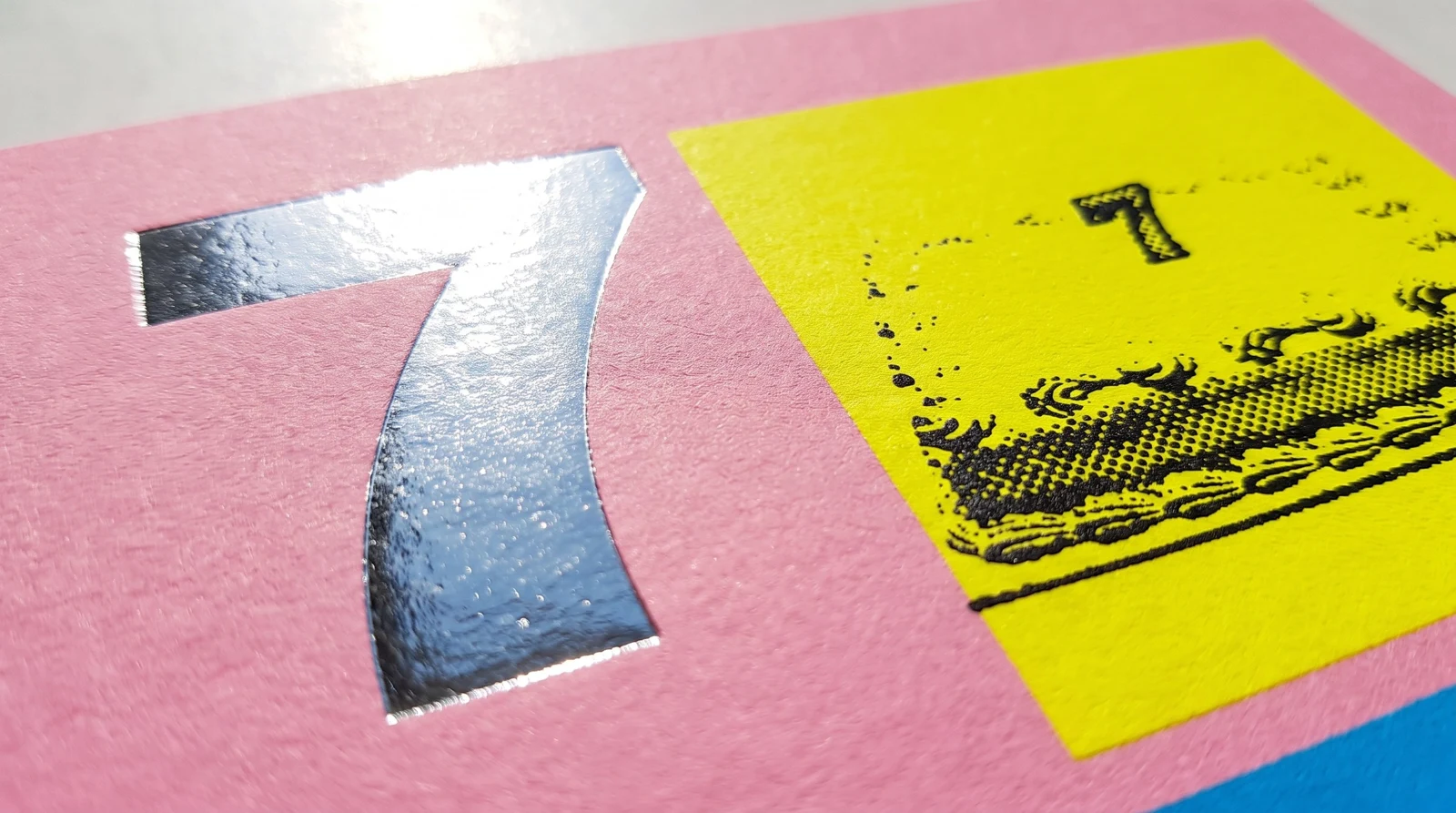 Macro of a mirror-silver foil 7 beside a fluorescent yellow square with an off-register black cake
