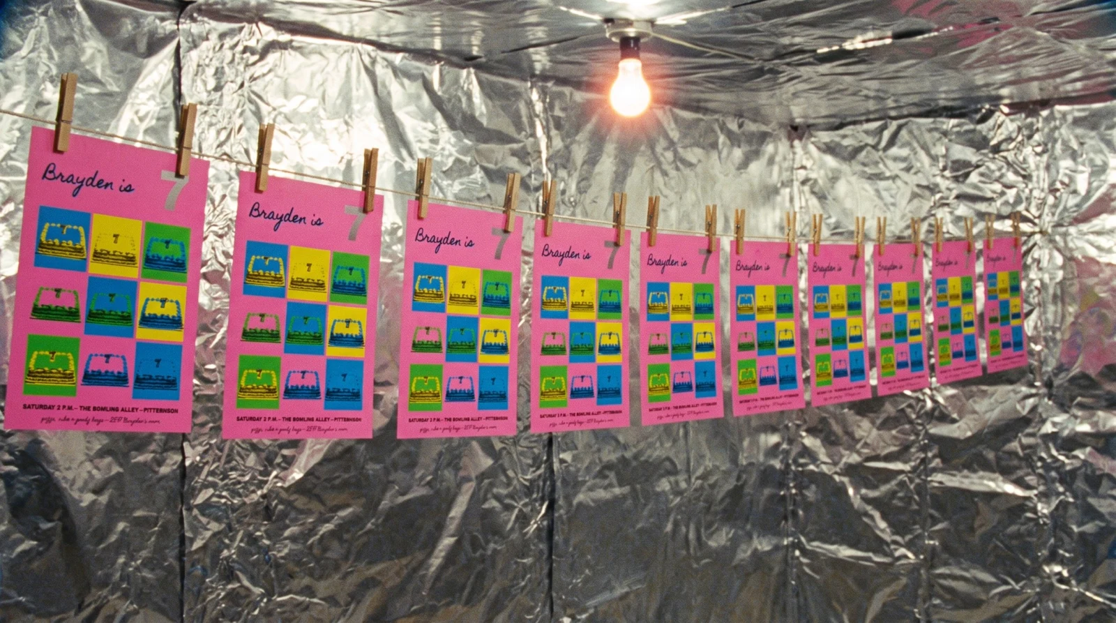 A row of identical pink posters drying on a line against crinkled silver foil walls