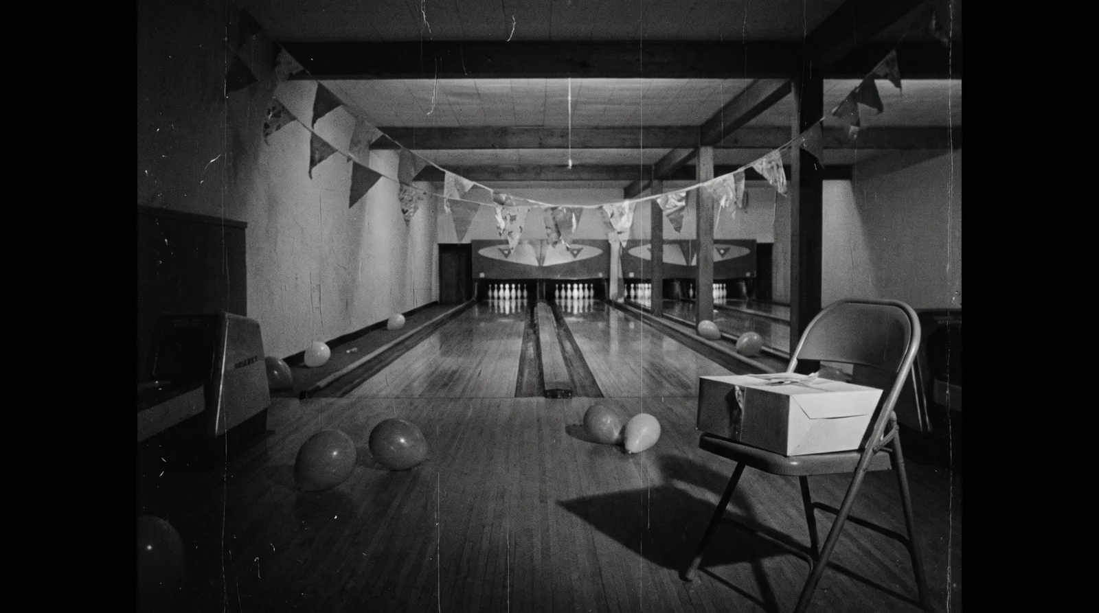 Black-and-white photograph of an empty bowling alley after the party, deflated balloons on the floor