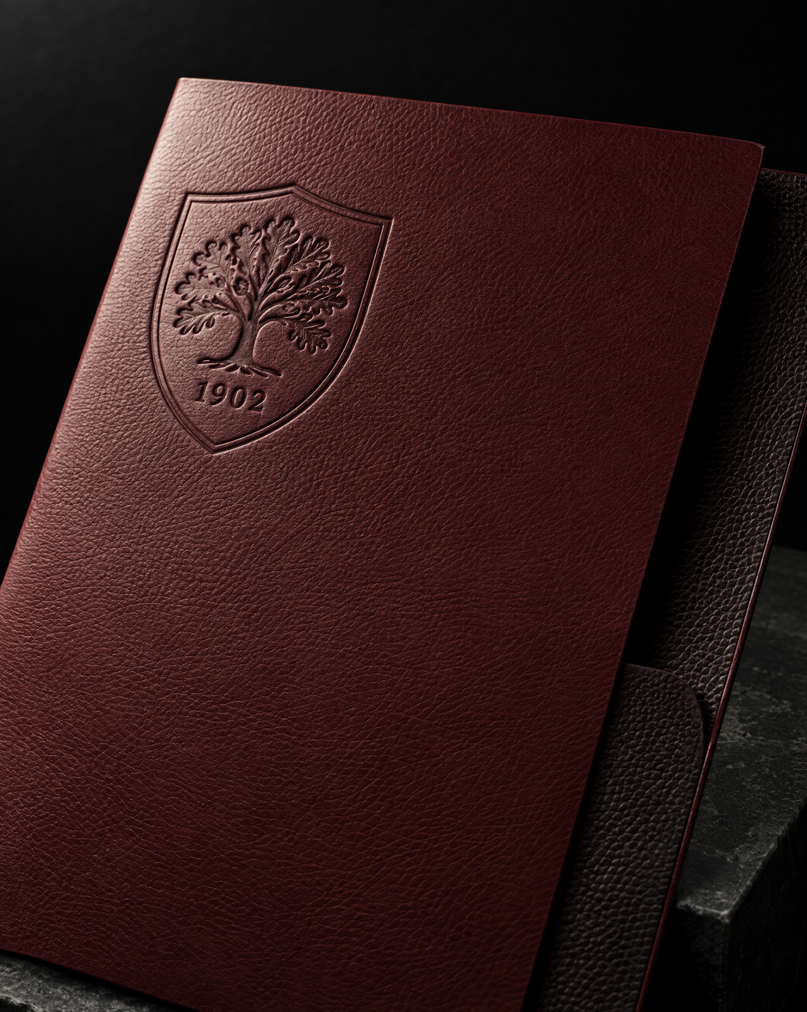 Oxblood leather-grain folder with a blind-debossed oak crest