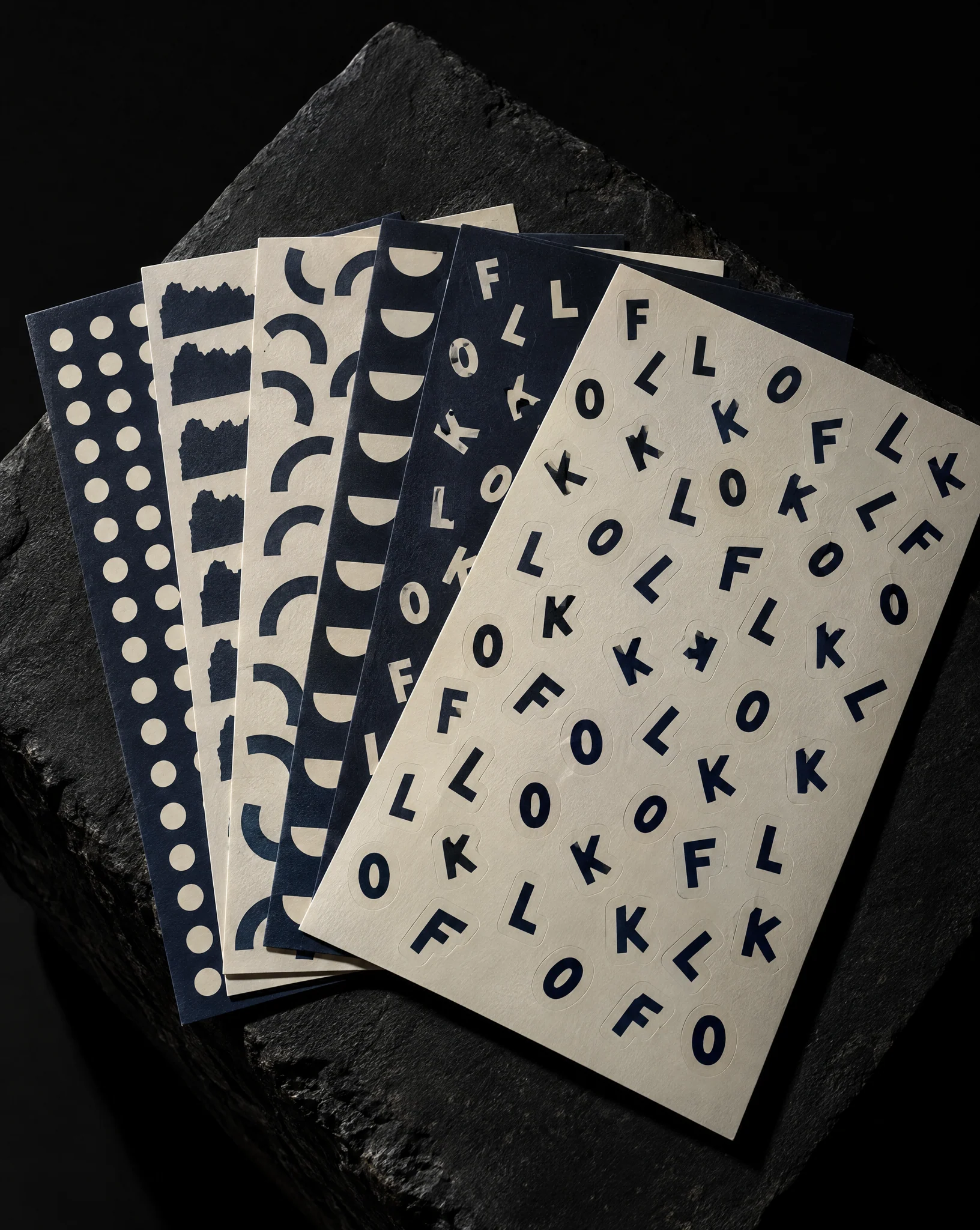 Navy and cream kiss-cut sticker sheets arranged on a black studio plinth