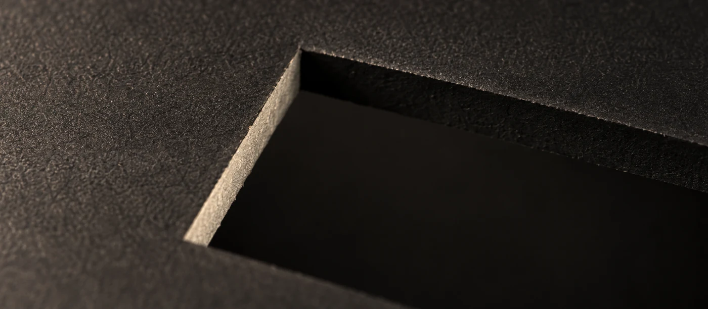 An interior die-cut aperture cut clean through matte black card, light falling through the opening.