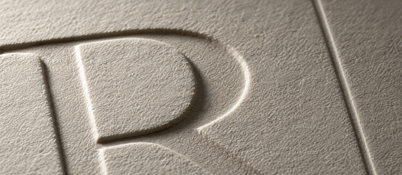 Blind letterpress impression in soft cotton paper, no ink, the design visible only as topography under raking light.