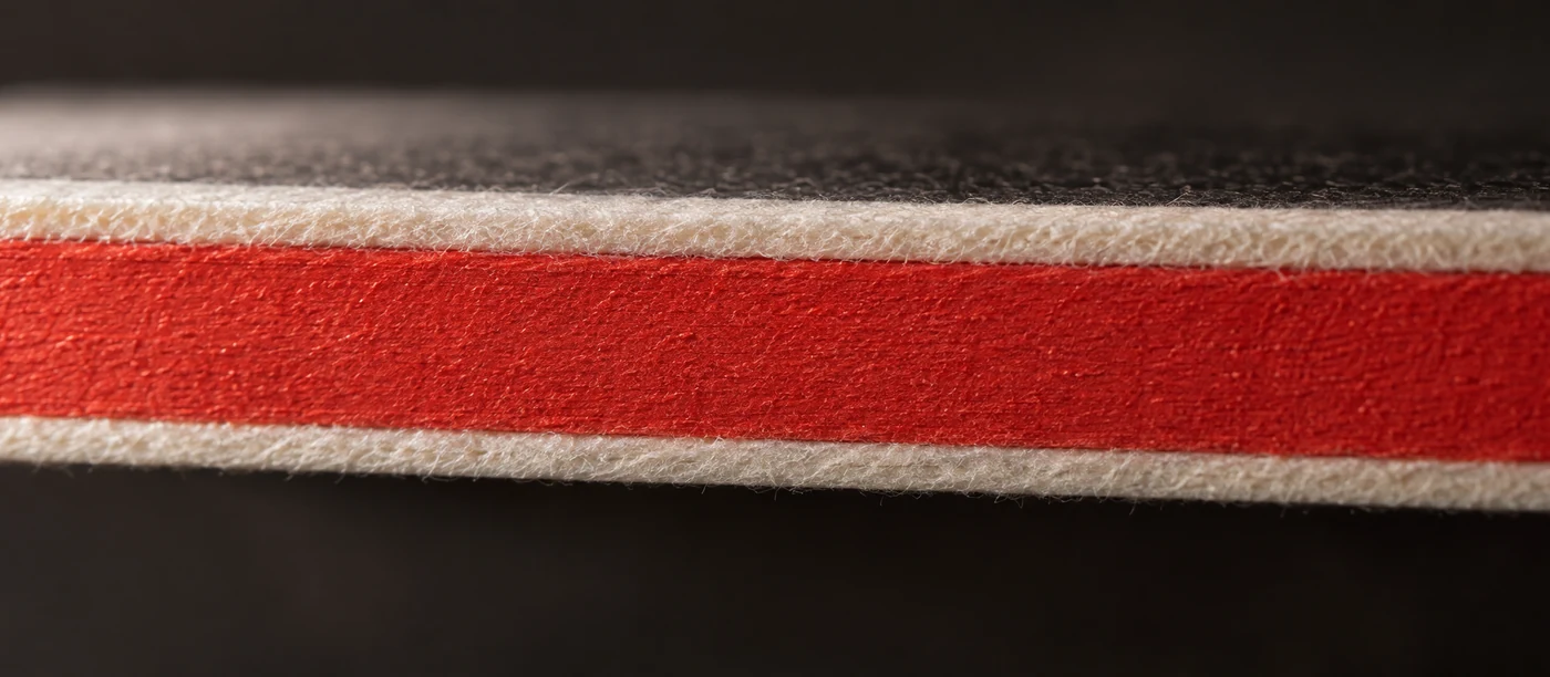 The edge of a duplex cotton card painted a solid coral red, showing full coverage across both bonded plies.