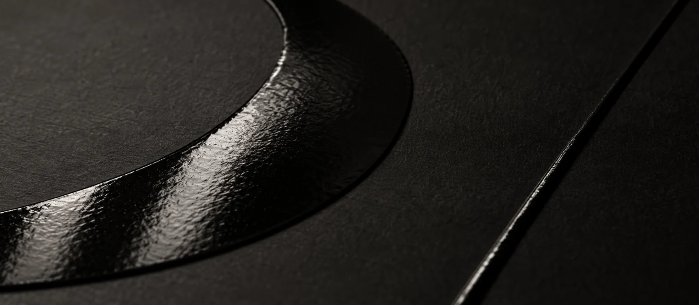 Raised gloss spot UV on matte black stock — same colour, different surface, separated only by how each holds the light.