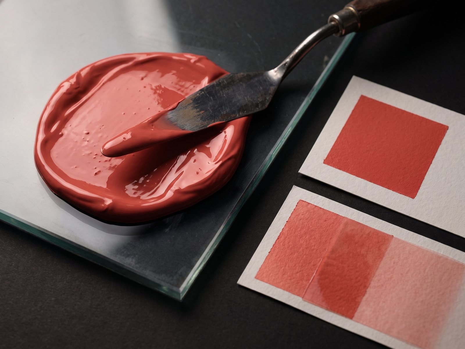 Hand-mixed coral spot ink on a glass slab beside paper drawdowns